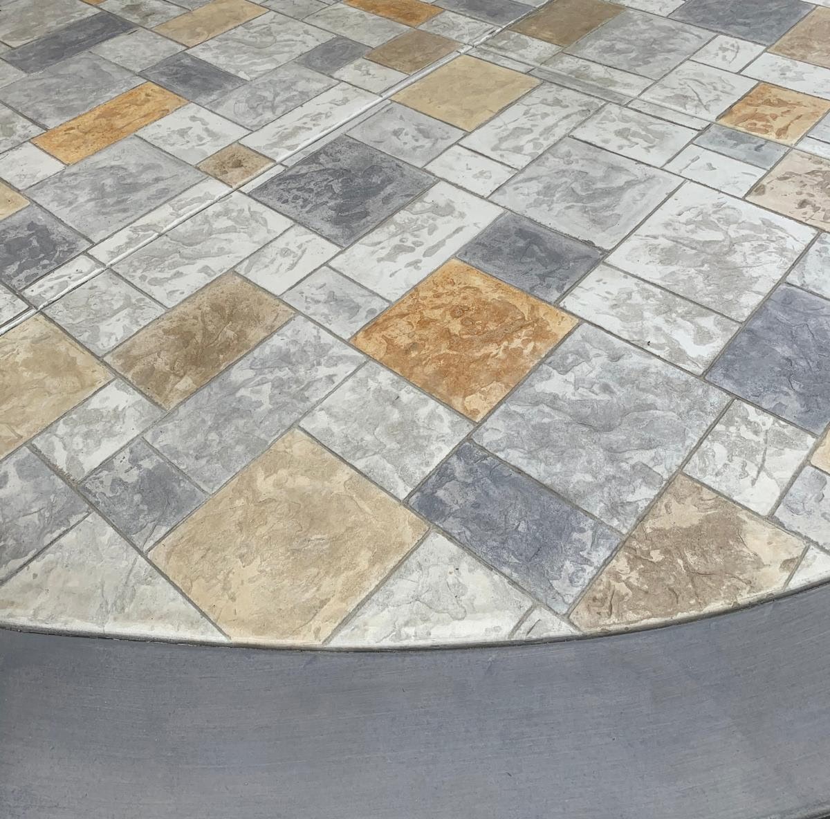 Decorative stamped concrete patio in mixed stone tones with a curved charcoal border